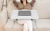 A person is sitting on a sofa with a laptop on a portable table placed on their lap. Produktbild-Vorschau