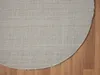 The back of a round, beige rug is shown on a wooden floor. Náhľad obrázku produktu