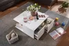 A white coffee table with open drawers, displaying a teddy bear and remote controls, placed on a rug in a living room setting. Voir les images du produit