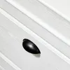 A close-up of a black drawer pull on a white wooden surface. Produktbild-Vorschau
