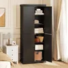 A black storage cabinet with its doors open, revealing shelves filled with folded clothes, bags, and boxes. A white nightstand with a lamp and picture frame is visible to the left. Voir les images du produit