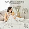 A woman is reading a book in bed, covered by a light gray blanket, with a fan and a vase of flowers in the background. Náhľad obrázku produktu