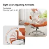 A person is sitting on an orange office chair with their legs crossed, demonstrating the chair's multi-positional armrests and footrest. A close-up inset shows the adjustable range of the armrests. Produktbild-Vorschau