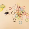 A collection of colorful metal rings and two keys on a light peach background. Produktbild-Vorschau