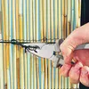 A hand using pliers to attach a wire to a bamboo fence. Produktbild-Vorschau