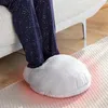 A person's legs wearing pajamas are inserted into a large, fluffy, white foot warmer that is placed on a rug next to a sofa. Red light emanates from the bottom of the foot warmer. Produktbild-Vorschau