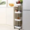 A narrow, multi-tier rolling storage cart filled with kitchen items, placed next to kitchen cabinets and a refrigerator. Náhled obrázku produktu