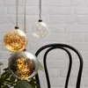 Three decorative glass balls with LED lights hanging in front of a white brick wall and a black chair. Produktbild-Vorschau