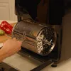 A hand is shown inserting a rotisserie basket into an air oven. Produktbild-Vorschau