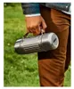 A person holding a silver thermos bottle outdoors. Voir les images du produit