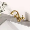 A vintage-style brass faucet is shown on a marble countertop next to a sink and a vase with greenery. Náhled obrázku produktu