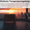 A black electric heater is placed on a dark wooden floor in front of a large window overlooking a city skyline at sunset. A sofa is visible on the right side of the image. Produktbild-Vorschau