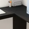 A close-up view of a black corner desk with a laptop and office supplies. Náhled obrázku produktu