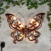 A decorative butterfly wall light with solar power, adorned with colorful jewels, mounted on a textured gray wall with ivy vines. Produktbild-Vorschau