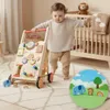 A baby is using a wooden walker in a nursery room. Produktbild-Vorschau