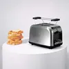 A stainless steel toaster and a stack of bread slices with butter on a white surface against a white background. Produktbild-Vorschau