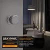 A smoke detector is mounted on a wall, with a living room scene in the background at night. Produktbild-Vorschau