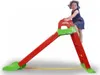 A young girl stands on a red and green plastic slide. Náhled obrázku produktu