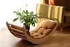 A wooden rocking chair with a brown cushion is placed on a wooden floor next to a potted plant and a green sofa. Produktbild-Vorschau