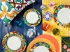 A colorful collection of tableware and decorative items arranged on a blue and yellow wooden surface. Anteprima dell’immagine prodotto