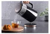 A hand is pouring hot water from a black electric kettle into a glass cup. A pastry is on a wooden board next to the cup. Náhled obrázku produktu