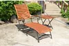 A wooden deckchair and a small side table are placed on a concrete patio next to lush green bushes and a wooden bridge. Produktbild-Vorschau