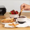 A hand dips a waffle stick into a bowl of chocolate sauce, with a bowl of strawberries and a waffle maker in the background. Podgląd zdjęcia produktu