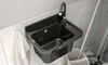 A black sink with a faucet is mounted on a tiled wall, with a white towel hanging to the left and cleaning tools in a bucket to the right. Náhled obrázku produktu