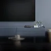A black Android TV box is placed on a blue media console in front of a large black television screen. Anteprima dell’immagine prodotto