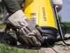 A person wearing gloves is shown connecting a cable to a yellow battery-powered sprayer. Podgląd zdjęcia produktu
