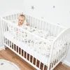 A baby is lying in a white crib with a patterned duvet and pillow. Produktbild-Vorschau