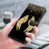 A hand holding a black phone case with golden angel wings and glitter design. Produktbild-Vorschau
