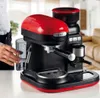 A person's hand is holding a glass next to a red and black espresso machine. Produktbild-Vorschau
