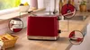 A red Bosch toaster is shown on a wooden kitchen counter, with close-up insets highlighting its features and a basket of toast nearby. Voir les images du produit
