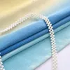 A close-up view of folded fabric with a string of pearls draped over it. Náhled obrázku produktu