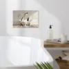 A canvas print of penguins in a bathtub is displayed on a wall above a bathtub in a bathroom. Produktbild-Vorschau