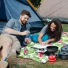 A couple is relaxing on a picnic blanket in front of a tent, with camping cookware nearby. Náhled obrázku produktu