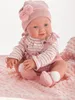 A baby doll dressed in pink clothing sits on a pink blanket. Anteprima dell’immagine prodotto