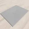 A flat, gray shower tray with a central drain cover, placed on a light wooden floor. Produktbild-Vorschau