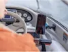 A person's hand is seen operating a boat's steering wheel and dashboard, with a smartphone mounted on a holder. Anteprima dell’immagine prodotto