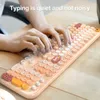 A person's hands typing on a pastel-colored keyboard with round keys. Produktbild-Vorschau