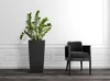A black planter with a green plant and a black chair in a room with white walls and a dark floor. Náhled obrázku produktu