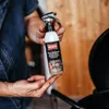 A person is holding a spray bottle of grill cleaner over an open grill. Produktbild-Vorschau