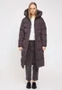 A woman is standing and posing in front of a white background, wearing a long puffer coat. Produktbild-Vorschau