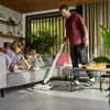 A man vacuums the floor in a living room while his two children read a book on the couch. Anteprima dell’immagine prodotto