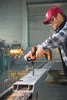 A man is using a cordless drill to drill into a metal beam in a workshop. Produktbild-Vorschau