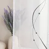 A close-up of a sheer curtain with a decorative embroidered pattern and a vase of lavender. Produktbild-Vorschau
