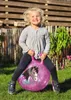 A young girl is happily bouncing on a glittery pink hopper ball with a horse design in a grassy outdoor setting. Produktbild-Vorschau