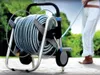 A person is using a hose reel in a garden setting. Podgląd zdjęcia produktu
