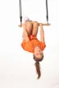 A young girl is hanging upside down on a wooden trapeze bar against a white background. Podgląd zdjęcia produktu